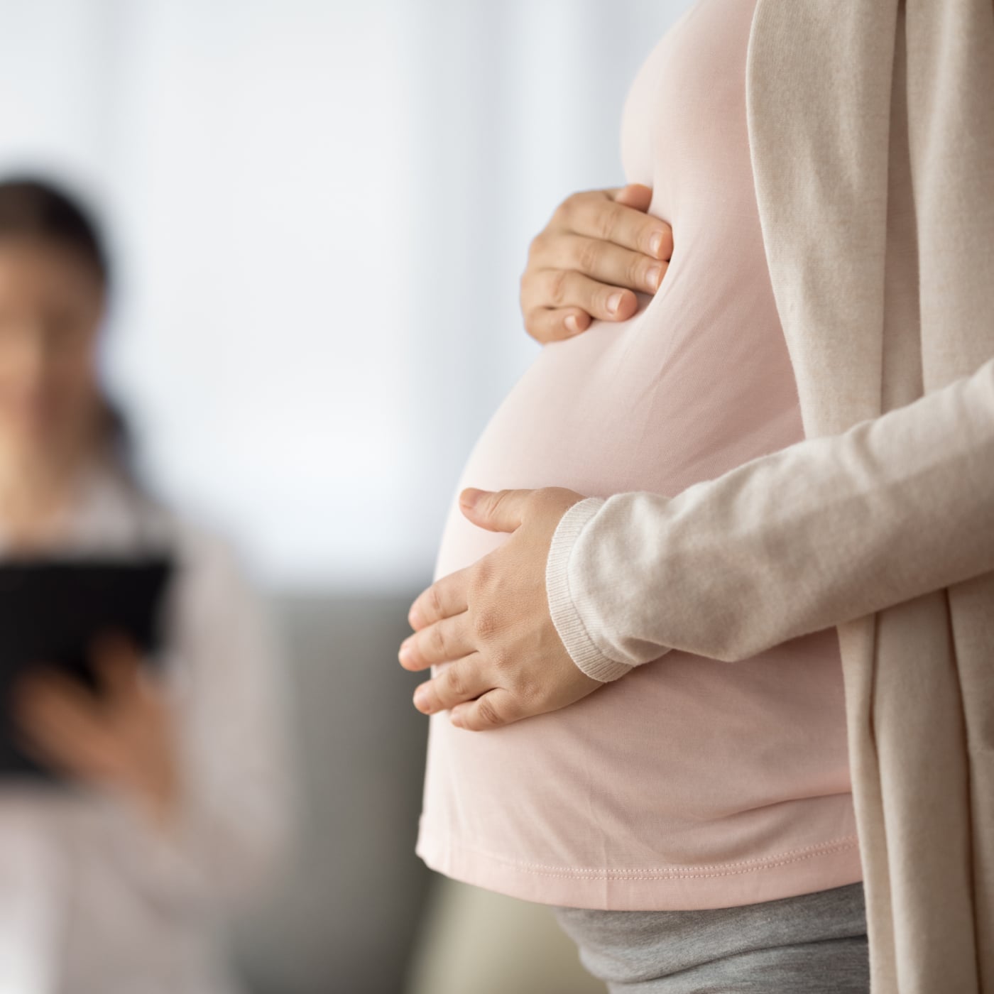 Pregnant person gently holding their belly in a bright home environment